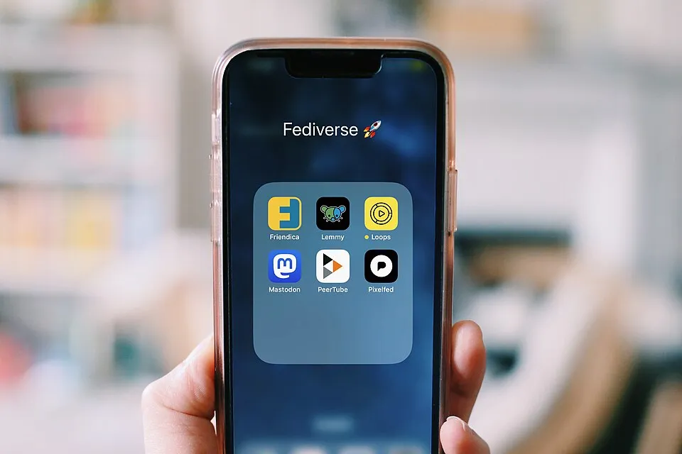  a photo of a hand holding a smartphone; on screen you see icons of Fediverse apps: Lemmy, Loops, Mastodon, PeerTube and Pixelfed by Elena Rossini